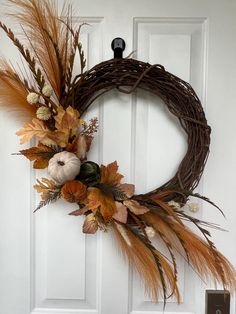 a wreath is hanging on the front door with dried flowers and pumpkins in it