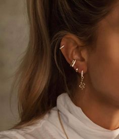 a woman wearing gold earrings and a white t - shirt is looking off to the side