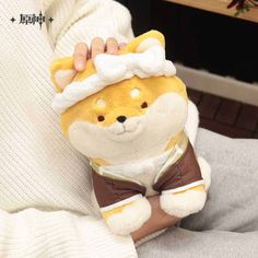 a person holding a small stuffed animal in their hand and wearing a white sweater with brown trims