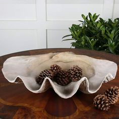 a wooden table topped with a white bowl filled with pine cones