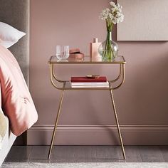 a table with books and vases on it in front of a pink wall next to a bed