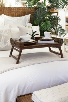 a tray with two cups on it sitting on top of a bed next to pillows