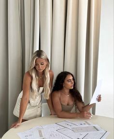 two women are sitting at a table looking at blueprints on the table in front of them