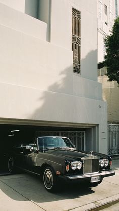 a black car parked in front of a white building with an open garage door on the side