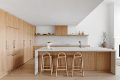 an open kitchen with wooden cabinets and bar stools in front of the counter top