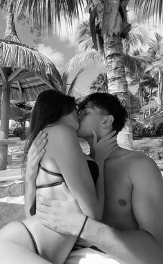 a man and woman kissing on the beach with palm trees in the backgroud