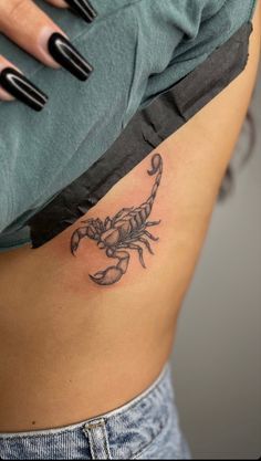 a woman's stomach with a small scorpion tattoo on her left side ribcage