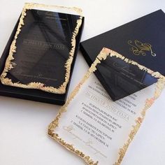 a black and gold wedding card with an ornate design on the front is laying next to it's box