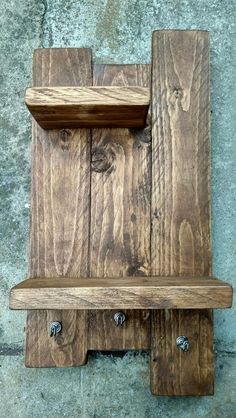 a wooden shelf sitting on top of a cement floor next to a stone wall with two hooks