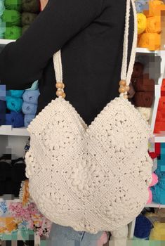 a woman carrying a white crocheted bag in front of a rack of yarn