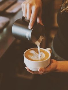 a person pouring coffee into a cup with the foam coming out of it's cappuccino