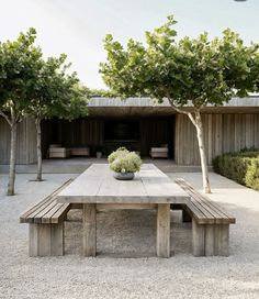 a wooden table sitting in the middle of a gravel covered ground next to trees and bushes