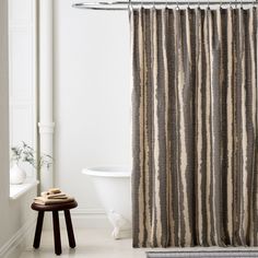 a white bath tub sitting next to a wooden stool in front of a shower curtain