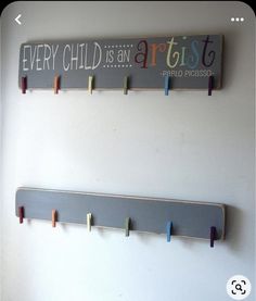 two wooden pegs are hanging on the wall next to a sign that says every child is an artist