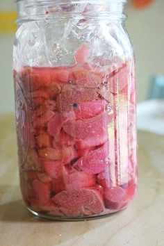 a jar filled with lots of cut up fruit sitting on top of a wooden table