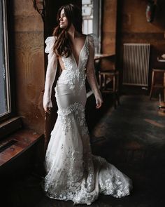 a woman in a wedding dress is standing near a window and looking off into the distance