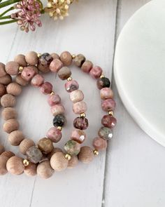 two bracelets made out of wood beads on top of a white table next to flowers