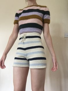 a woman in striped shorts is standing with her hands behind her back and looking at the camera