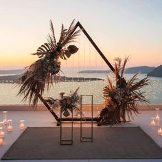 a table with candles and flowers on it near the water at sunset or dawn in an outdoor setting