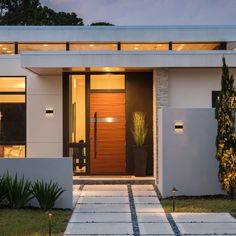 a modern house is lit up at night with lights on the front door and side windows