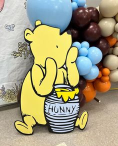 a winnie the pooh balloon sitting on top of a bucket filled with blue and yellow balloons