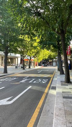 an empty city street with trees lining the sides and yellow lines painted on the road