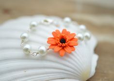 an orange flower and pearl bracelet on a shell