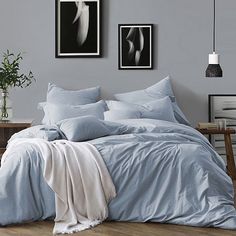 a bed with blue sheets and pillows in a room next to pictures on the wall