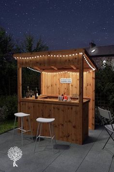 an outdoor bar is lit up at night with string lights on the roof and two stools