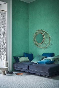 a living room with green walls and blue couch in the middle, surrounded by pillows