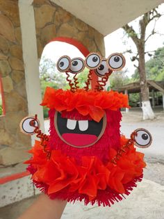 a hand holding up a red stuffed animal with googly eyes