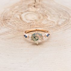 a gold ring with three stones on it sitting on top of a tree stump in the woods