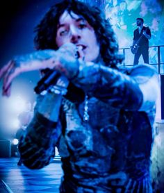 a man with long hair holding a microphone in front of his face while standing on stage