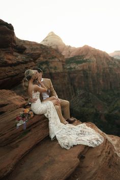 a bride and groom sitting on the edge of a cliff