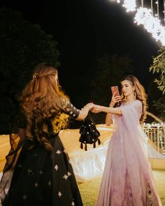 a woman in a pink dress is taking a photo with her cell phone while standing next to another woman