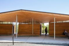 two people sitting on a bench in front of a wooden structure with columns and poles