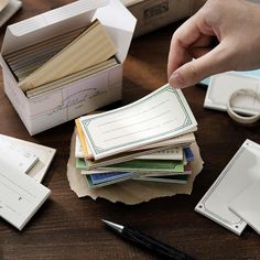 a person holding a piece of paper next to many other papers on a table with scissors and pens