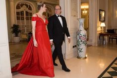 a man and woman in formal wear standing next to each other near a vase on the floor