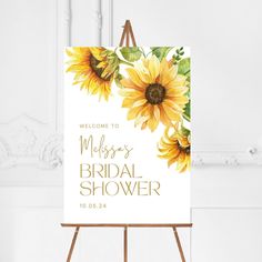 a welcome sign with sunflowers on it in front of a white wall and wooden easel