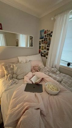 a bed with a laptop and bowl of popcorn on it in front of a window