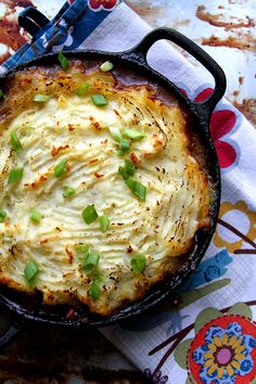 a baked dish in a cast iron skillet on a colorful tablecloth with flowers