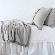 a white bed with two pillows and some blankets on it's headboard, in front of a white wall