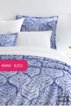 a bed covered in blue and white leaves with a pink price tag on the pillow