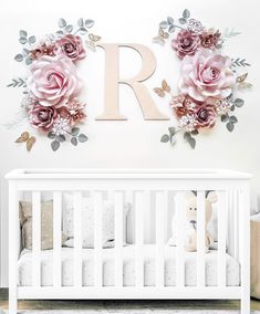 a white crib with pink flowers on the wall and a wooden letter r above it