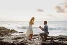 a man kneeling down next to a woman on top of a rocky cliff near the ocean