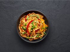 a bowl filled with noodles and vegetables on top of a black table next to chopsticks