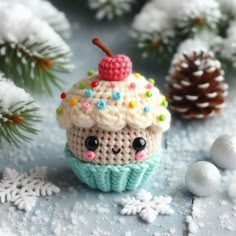 a crocheted cupcake with a cherry on top sitting next to pine cones