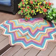 a colorful crocheted blanket sitting on top of a wooden deck next to potted plants