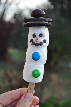 a hand holding a marshmallow snowman on a stick