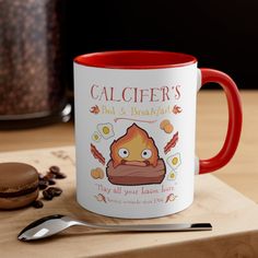 a red and white coffee mug sitting on top of a wooden table next to a cookie